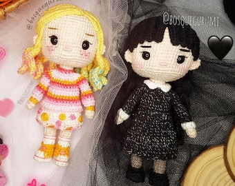 May include: Two handmade crochet dolls. One doll has blonde hair and wears a pink, orange, and white striped sweater and a white skirt with yellow polka dots. The other doll has black hair and wears a black dress with a white collar.