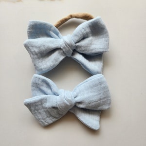 May include: Two light blue fabric hair bows with a knotted centre. The bows are attached to elastic headbands.
