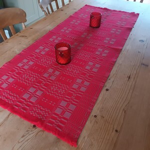 May include: A red table runner with a white geometric pattern. Two red glass candle holders are placed on the runner.