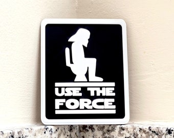 Könnte beinhalten: Ein schwarz-weißes Schild mit einer Silhouette einer Person, die auf einer Toilette sitzt. Das Schild sagt "Use the Force".