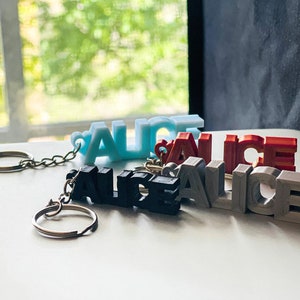 May include: Four keychains with the name "Alice" spelled out in 3D letters. The keychains are in blue, black, red, and gray.