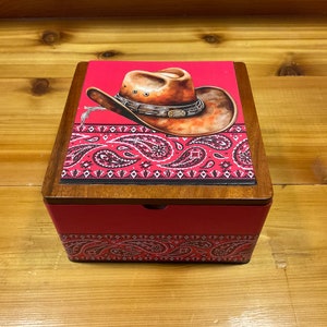 May include: A red wooden box with a paisley pattern and a cowboy hat on the lid. The box has a hinged lid and a small latch.