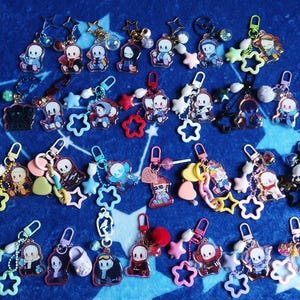 Könnte beinhalten: Eine Sammlung bunter Schlüsselanhänger mit Cartoon-Charakteren. Die Schlüsselanhänger haben verschiedene Designs, darunter Sterne und Herzen, und sind an Metallverschlüssen befestigt. Die Charaktere sind in verschiedenen Outfits und Posen dargestellt, mit einer Vielzahl von Farben.