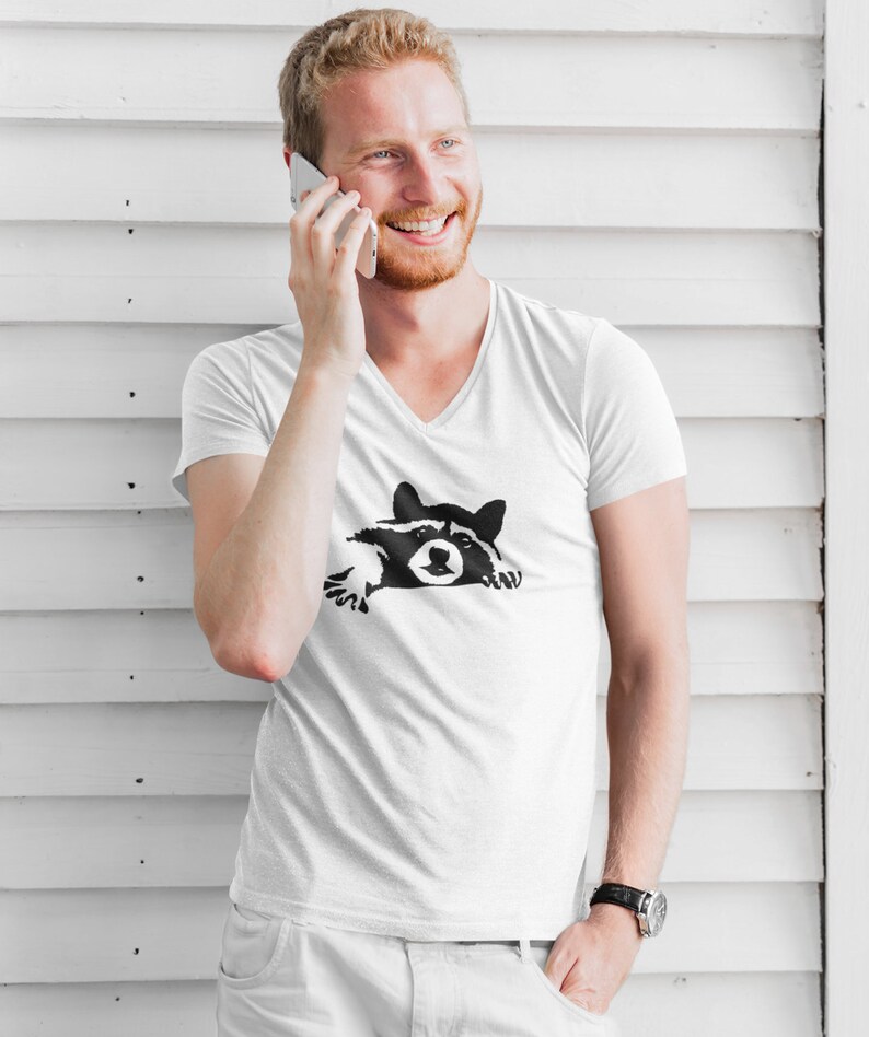 May include: A white V-neck t-shirt with a black and white graphic of a raccoon peeking out from behind a wall.