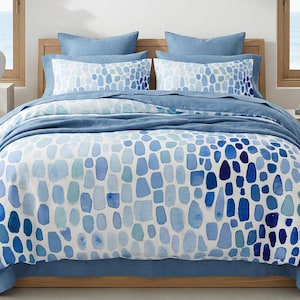 May include: A bed with a blue and white patterned duvet cover and matching pillowcases. The pattern features an abstract design of blue shapes on a white background. The bed is made up with a blue sheet and a blue throw blanket. The room has a coastal theme.