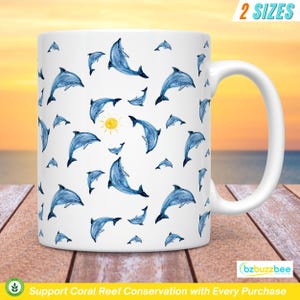 May include: White ceramic mug with a blue and white dolphin pattern. The mug has a handle and a yellow sun in the center. The text "Support Coral Reef Conservation with Every Purchase" is at the bottom of the mug.