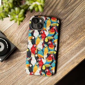 Puede incluir: Una funda de teléfono colorida con un patrón de loros y tucanes. La funda es negra con una variedad de colores brillantes, incluyendo rojo, amarillo, azul, verde y naranja.