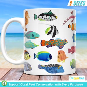 May include: White ceramic mug with a colorful design of various tropical fish, including a blue and black fish, a yellow and orange fish, and a red and white fish. The mug has a handle and the text "2 SIZES" and "Support Coral Reef Conservation with Every Purchase" is printed on the mug.