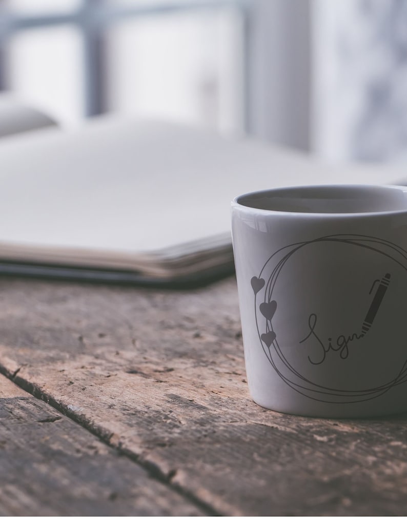 May include: White ceramic mug with a black and gray design. The design features a circle with a pencil and the word "Sign" written in cursive. There are four small hearts around the circle.