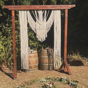 May include: A wooden archway decorated with a white macrame hanging. Two wooden barrels are placed in front of the archway.