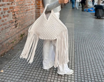 May include: A white crocheted tote bag with long fringe. The bag is made of thick cotton rope and has a wide, open top.