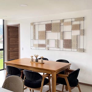 May include: A dining room set featuring a rectangular wooden table with six black velvet chairs. A decorative wall art piece with woven squares in neutral tones hangs above the table. Small vases with decorative stems sit on the table.