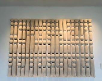 May include: A wall hanging composed of multiple vertical strands of off-white fiber. Each strand features a series of rounded, bulbous shapes created by wrapping the fiber, separated by thin black bands, ending in straight, loose fringe at the bottom.