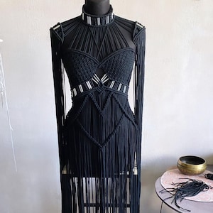 May include: A black macrame dress with a high neckline and long sleeves. The dress features a geometric pattern and is decorated with silver accents.