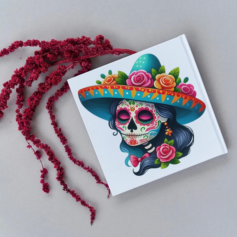 May include: A white notebook with a colorful illustration of a Day of the Dead sugar skull wearing a blue sombrero with red, pink, and yellow flowers. The skull has a sugar skull design with pink cheeks and blue eyes.