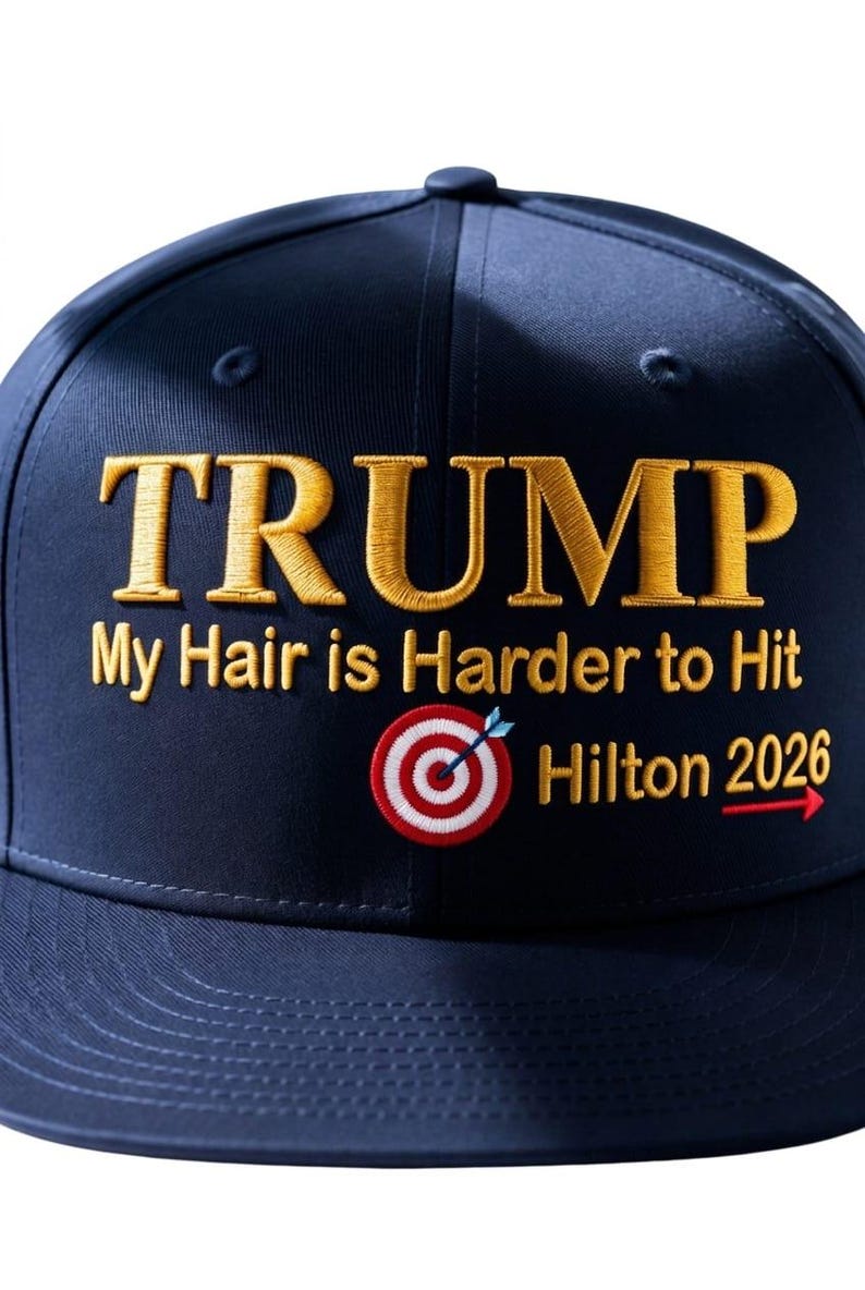 May include: Navy blue baseball cap with gold embroidered text reading "TRUMP" above the phrase "My Hair is Harder to Hit". A target graphic and "Hilton 2026" are also embroidered.