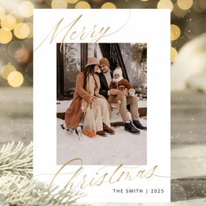 May include: A Christmas card with a family photograph. The card has gold script that reads "Merry Christmas" and "The Smith | 2025". The family is seated on a snowy porch, creating a festive scene.