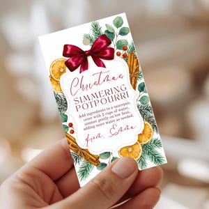 May include: A festive gift tag with a burgundy bow, displaying the text "Christmas Simmering Potpourri." The tag is adorned with watercolour illustrations of orange slices, cinnamon sticks, and sprigs of foliage.