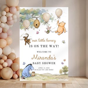 May include: A baby shower welcome sign featuring Winnie the Pooh characters. The sign includes the text "our little honey is on the way!" and "Miranda's Baby Shower". The sign is decorated with balloons, butterflies, and a honey pot.