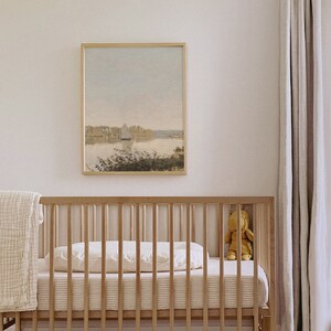 May include: A wooden crib with a white mattress and a white blanket. A framed painting of a lake with a sailboat hangs on the wall above the crib. A stuffed animal sits on the crib.