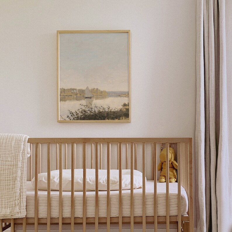 May include: A wooden crib with a white mattress and a white blanket. A framed painting of a lake with a sailboat hangs on the wall above the crib. A stuffed animal sits on the crib.