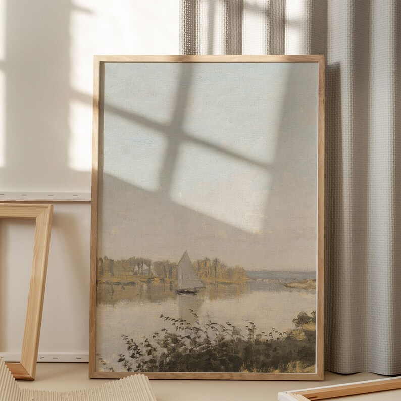 May include: A framed painting of a landscape with a sailboat on a lake. The painting is in a light wood frame and has a soft, muted color palette.