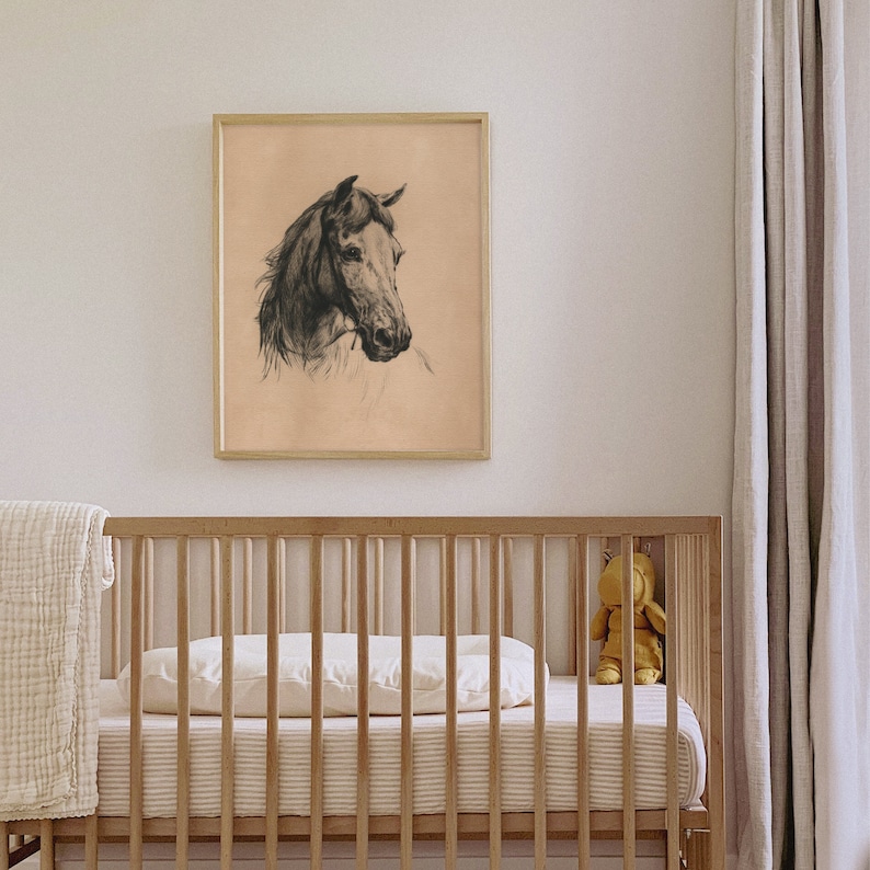 May include: A black and white drawing of a horse's head in a light brown frame hanging above a wooden crib with a white mattress and a stuffed animal.