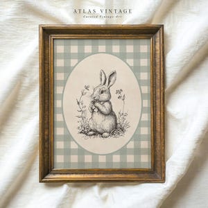 Puede incluir: Una impresión enmarcada con un fondo de cuadros verdes y blancos. La impresión presenta una ilustración en blanco y negro de un conejo sentado en un campo de flores. El texto "ATLAS VINTAGE Curated Vintage Art" está en la parte superior de la impresión.