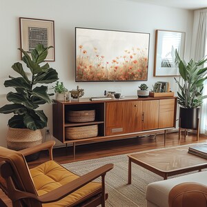 Może przedstawiać: Salon w stylu mid-century modern z drewnianym kredensem, dużym telewizorem i rośliną w doniczce. Kredens ma jasne wykończenie z drewna i posiada dwie drzwi oraz p&oacute;łkę. Telewizor jest zamontowany na ścianie nad kredensem i wyświetla scenę z natury. Roślina to duża, zielona roślina w brązowej doniczce. Pok&oacute;j jest urządzony dywanem, stolikiem kawowym i fotelem.