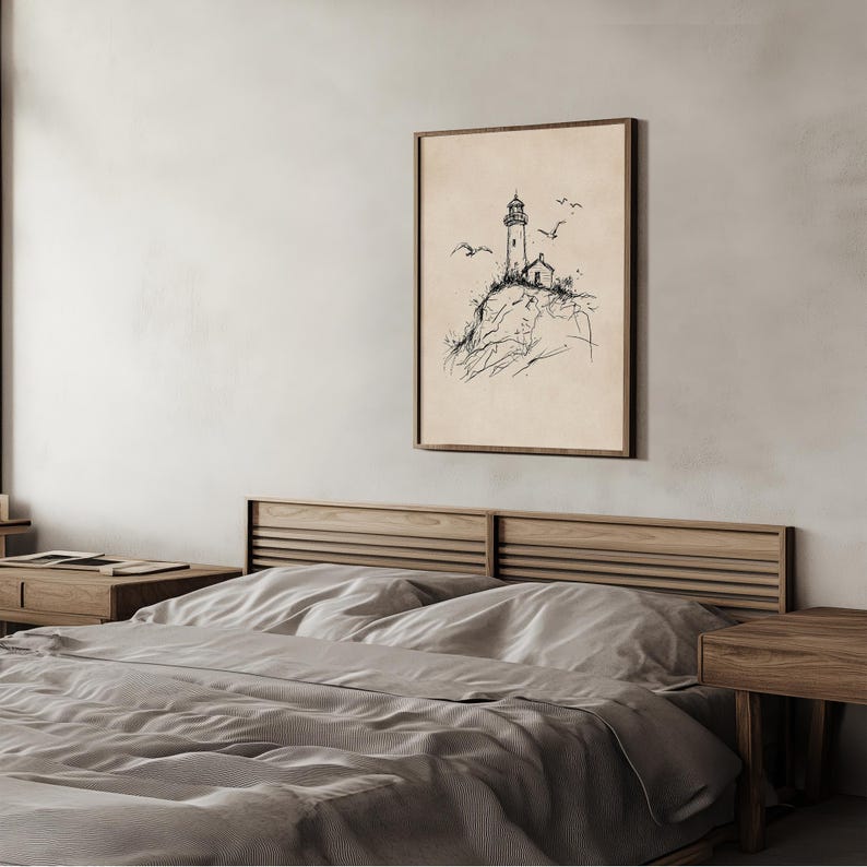 May include: A framed art print featuring a pen and ink drawing of a lighthouse on a rocky cliff, with seagulls in flight. The artwork is set against a beige background and framed in a dark wood. The print is displayed above a bed.