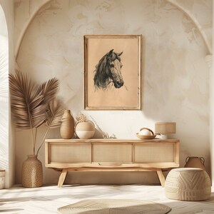 May include: A framed black and white drawing of a horse's head, hanging on a wall above a light wood cabinet with a woven rattan front. The cabinet is decorated with a vase and a bowl.
