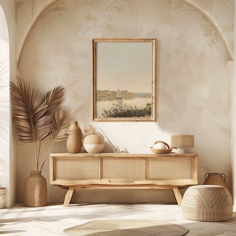 May include: A light wood console table with three drawers and a woven rattan front. The table is decorated with two ceramic vases, a woven basket, and a framed landscape painting. The table is set against a light beige wall with a subtle archway.