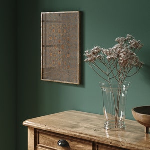 May include: A wooden dresser with three drawers, a vase with dried flowers, and a framed artwork with a geometric pattern. The dresser is made of light brown wood and has a natural finish. The vase is clear glass and the flowers are white. The artwork is framed in gold and has a dark background with a gold pattern.