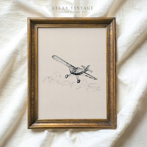 Puede incluir: Un dibujo en blanco y negro de un pequeño avión volando sobre las nubes. El dibujo está enmarcado en un marco dorado y lleva el título "ATLAS VINTAGE Arte vintage seleccionado".
