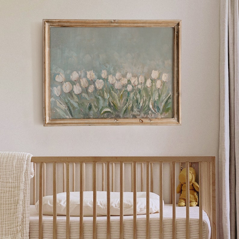 May include: An oil painting of white tulips in a gold frame hangs above a wooden cot. The cot has a striped mattress, a white pillow, and a yellow teddy bear. A cream blanket is draped over the side of the cot.