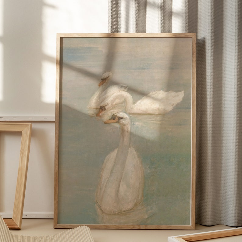May include: A framed painting of three white swans swimming in a body of water. The swans are depicted in a soft, muted palette of blues and greens, creating a serene and tranquil scene.