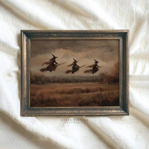 Könnte beinhalten: Gerahmtes Vintage-Gemälde, das drei Hexen auf Besen zeigt, die über ein Feld fliegen. Das Kunstwerk verwendet eine gedämpfte Farbpalette aus Braun-, Beige- und Grautönen mit einem dunklen, verzierten Rahmen. Der Text "ATLAS VINTAGE Curated Vintage Art" ist sichtbar.