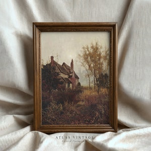 May include: A framed vintage print depicting a cottage in a rural setting. The cottage is red brick with a thatched roof and is surrounded by trees and tall grass. The sky is a soft blue with a hint of mist.
