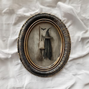 Pode incluir: Uma obra de arte emoldurada oval com um chapéu de bruxa, capa, vassoura e sacola, com uma silhueta de morcego. A moldura tem um design texturizado em preto e dourado. A obra de arte é definida em um fundo neutro, evocando o tema do Halloween.