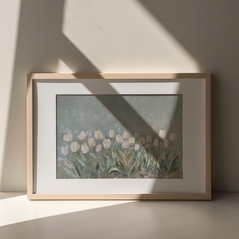 May include: A framed painting of white tulips in a field. The artwork features a light blue background and green foliage, with a natural wood frame and white mount. The painting is lit by natural light.