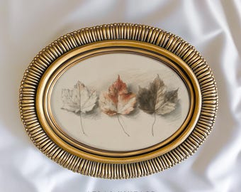 May include: An oval, gold-colored framed artwork featuring three detailed leaf illustrations in shades of white, red, and brown. The frame has a textured, ridged design. The text "ATLAS VINTAGE Curated Vintage Art" is at the bottom.