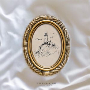 May include: Oval gold-toned frame with a sketch of a lighthouse on a cliff, with seagulls in flight. The artwork is in black and white. The frame has a textured, ridged border. The text "ATLAS VINTAGE" is at the bottom.