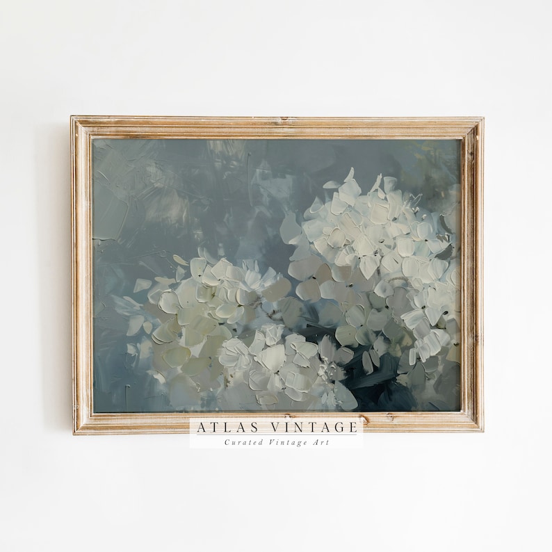 May include: A framed painting of white hydrangeas against a blue-grey background. The painting is in a light wood frame and has the text "ATLAS VINTAGE Curated Vintage Art" at the bottom.