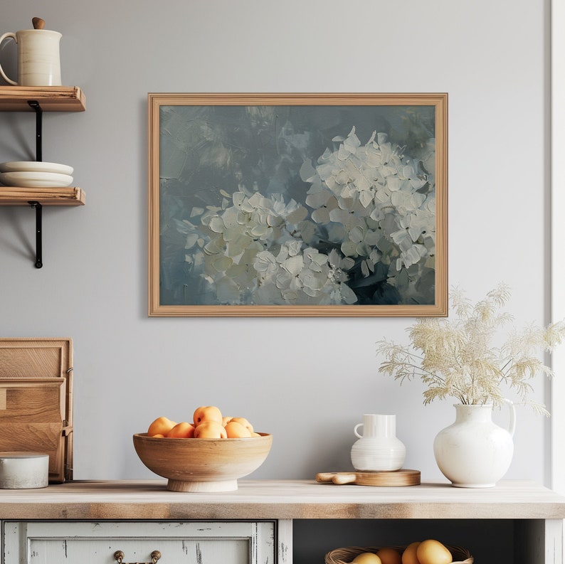May include: A framed painting of white hydrangeas against a blue background. The painting is in a light wood frame and is hanging on a white wall.