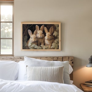 Pu&ograve; includere: Una stampa incorniciata con tre adorabili conigli marroni tra il fogliame. L'opera d'arte &egrave; incorniciata in una cornice di legno chiaro e appesa sopra un letto con lenzuola e cuscini bianchi. L'immagine cattura un tema sereno ispirato alla natura.
