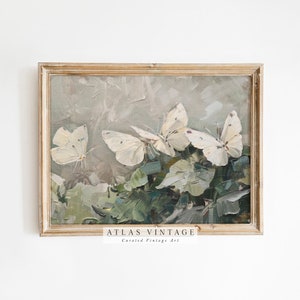Może przedstawiać: Wizerunek vintage przedstawiający trzy białe motyle na tle zielonych liści. Obraz jest oprawiony w jasną drewnianą ramę. Tekst "ATLAS VINTAGE Curated Vintage Art" znajduje się na dole ramy.