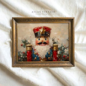 Puede incluir: Una pintura vintage enmarcada de un cascanueces con un uniforme rojo, blanco y azul. El cascanueces está rodeado de follaje verde y bayas rojas. La pintura está en un marco dorado con el texto "ATLAS VINTAGE Curated Vintage Art" en la parte superior.