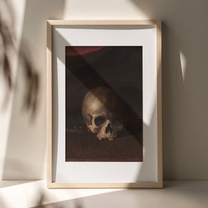 May include: A framed print of a still life featuring a human skull in a dark setting. The skull is white with visible teeth and eye sockets. The background is a dark brown color.