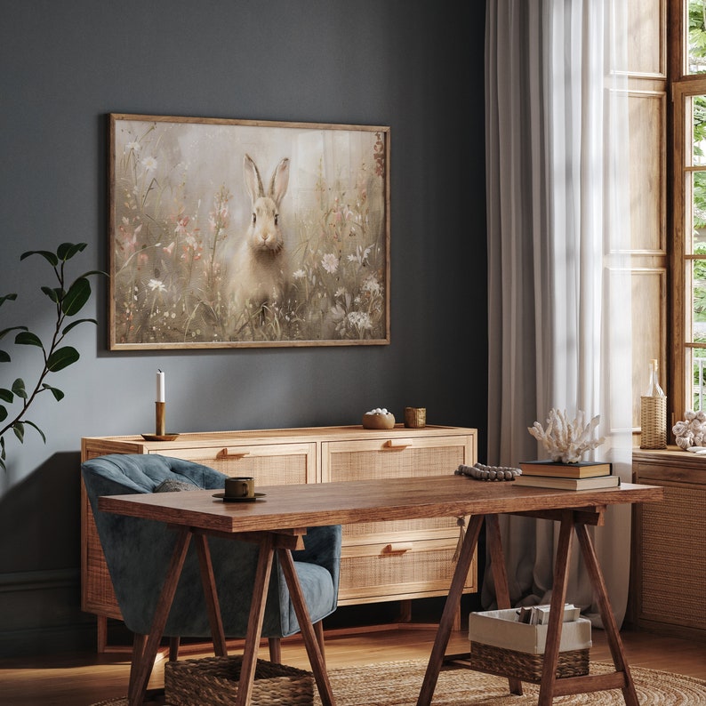 Puede incluir: Una impresi&oacute;n enmarcada de un conejo blanco en un campo de flores. La impresi&oacute;n est&aacute; colgada en una pared gris oscuro sobre una c&oacute;moda de madera con tres cajones. Una silla azul se encuentra frente a la c&oacute;moda, y una mesa de madera con una silla azul se encuentra frente a la c&oacute;moda.