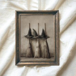 May include: A framed vintage art print depicting three witch hats and brooms. The artwork has a sepia tone and a dark brown frame. The image is set against a neutral background, creating a classic Halloween theme. The print is a vintage style.